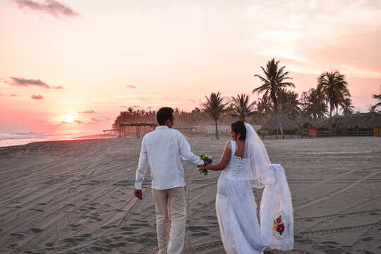 novios caminando en la orilla de la playa en un atardecer de boda romantica