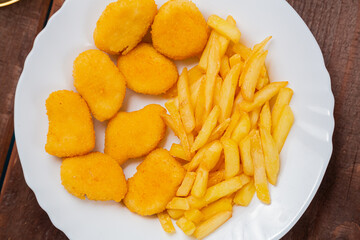 French fries and golden nuggets with cheese sauce on a plate close-up