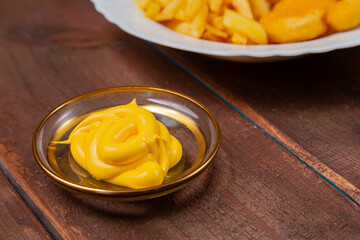 French fries and golden nuggets with cheese sauce on a wooden table fragment