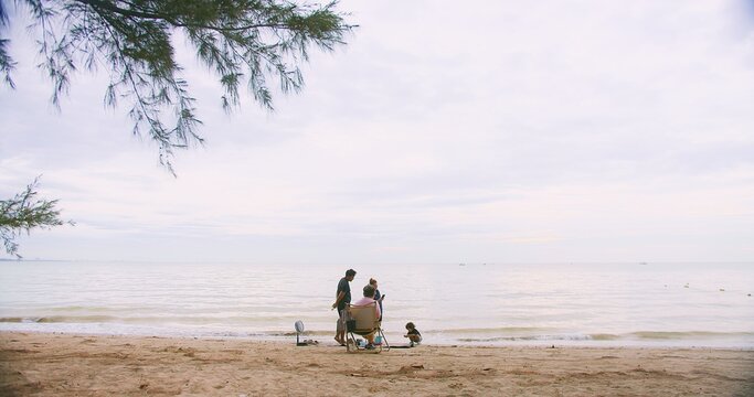 happy Asian family relaxing on a tranquil beach, enjoying the ocean view under a cloudy sky, Multi-generation family enjoy outdoor together at summer travel holiday vacation time