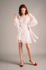 Broderie mini dress in white. Romantic studio portrait of ginger woman on red high heels. Summer...