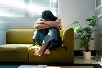 Young woman suffering from depression sitting on sofa hugging knees at home