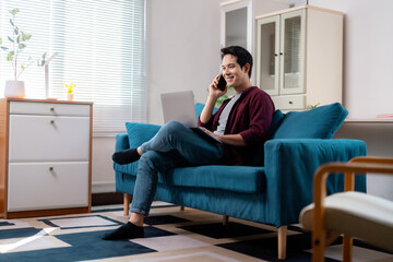 Fototapeta premium Asian Freelancer Talking on Phone and Working on Laptop at Home
