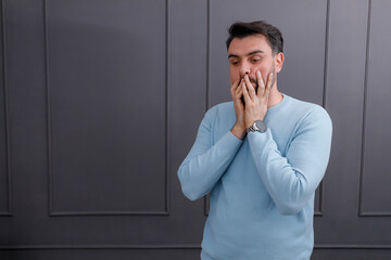 Man expressing deep thought while standing against a dark wall in a casual blue sweater at a quiet...