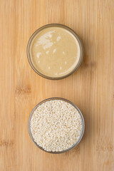 Sesame seeds and paste, sesame sauce in a glass bowl on a wooden surface. Top view.