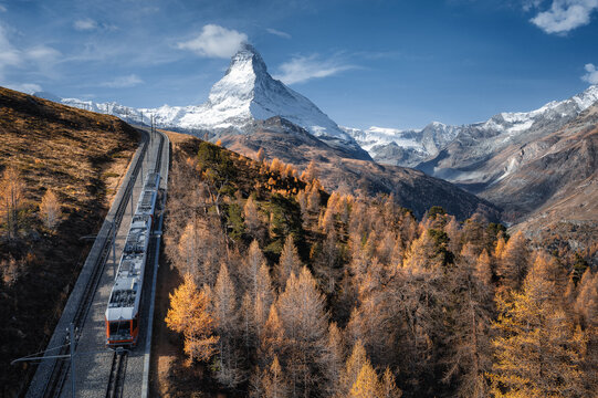 Aerial view of majestic peak of Matterhorn with yellow larch trees and swiss train Gornergrat Bahn in the foreground during a sunny autumn day in swiss alps. Zermatt, Switzerland.