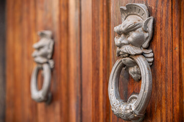 two antique metal door knockers goblin or demon faces biting a large ring. on rustic wooden door, the aged patina and intricate details enhance its gothic and vintage charm, sense of power protection 