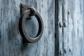 antique metal ring door knocker on a weathered blue wooden door. The aged patina and rustic texture...
