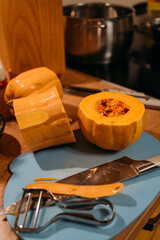 Cooking a homemade pumpkin dinner. The pumpkin is cut into three pieces, lying on a cutting board. There are many different kitchen utensils on the table