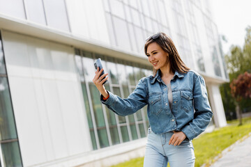 Obraz premium Woman Takes a Selfie With Her Phone in Front of a Modern Building 
