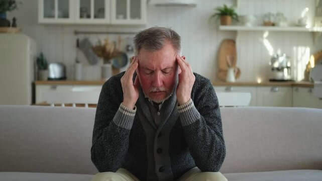 Headache pain. Unhappy middle aged senior man suffering from headache sick rubbing temples at home. Mature old senior grandfather touching temples experiencing stress. Man feeling pain hurt in head