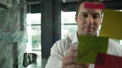 Portrait of professional male leader writing marketing idea on sticky notes. Caucasian businessman...