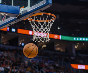 Fototapeta premium Slam Dunk Moment: A basketball, suspended in mid-air, streaks towards the net as it captures the intensity of a sporting event. The image exudes dynamism, emphasizing the perfect harmony of sport.