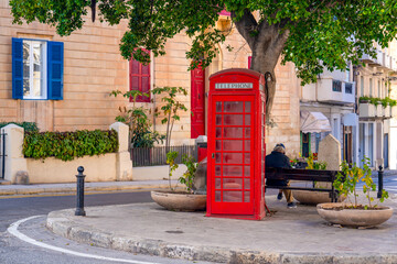 Malta, a man sits next an old red english telephone cabine  at a roundabout in Valetta.
