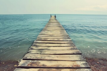 Obraz premium Long wooden pier extending into calm turquoise waters under a clear sky on a sunny day
