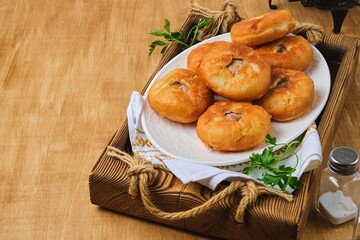 Belyashi, deep-fried round pies made of yeast dough with minced meat and onion filling on a white plate on a wooden tray. Deep-fried pastries.