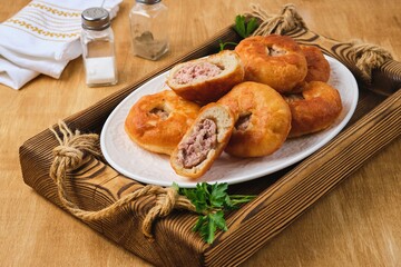 Belyashi, deep-fried round pies made of yeast dough with minced meat and onion filling on a white plate on a wooden tray. Deep-fried pastries.