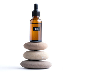 Essential oil in glass bottle on stack of stones on white background.