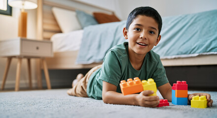 Young boy lying on the floor of his bedroom, happily playing with colorful building blocks, developing creativity and fine motor skills