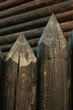 Wooden log fence against the background of the house wall.