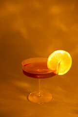 glass of champagne with a slice of orange on an orange background, with shadows