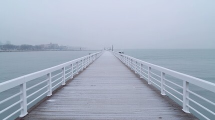 Obraz premium Snowy pier extending into misty sea, coastal city background; winter travel