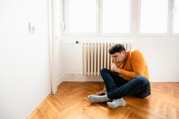 Fototapeta premium Young man sitting alone in front of radiator and coughing