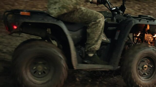 Muddy trail, ATV adventure, Helmet journey. Individual in camo clothing and helmet pilots ATV through muddy forest, kicking up mud and water.