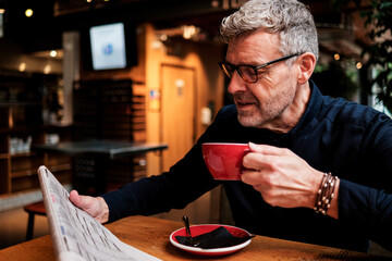 Senior businessman enjoying morning coffee and reading newspaper at cafe