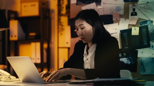 Asian female detective works on her laptop, feeling overwhelmed by the case