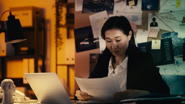 Asian female police detective reviews evidence documents while working on a case