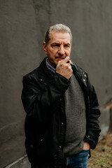 Fototapeta premium Man thoughtfully pondering against a grey wall in an urban setting