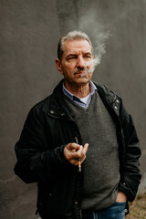 Mature man smoking in casual attire against a textured wall