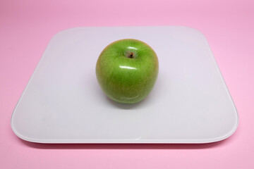 Fresh green apple on a white scale against a pink background