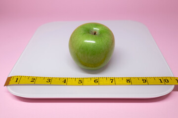 Green apple on white scale with measuring tape for scale