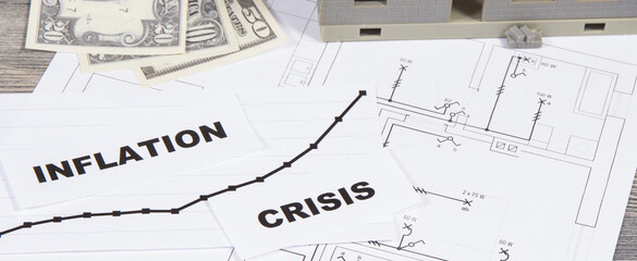 Inscriptions crisis and inflation, currencies Dollar, toy house under construction on electrical diagrams of house. High prices of real estate, building or rent home