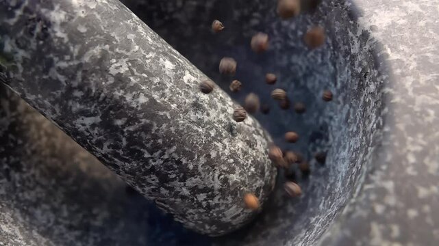 Spicy black peppercorns are falling into the grey stone mortar in slow motion. High quality 4k footage