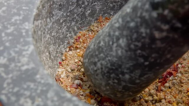 Hand with a pestle is grinding and mixing various kinds of spices, peppers and sea salt in the grey stone mortar. High quality 4k footage
