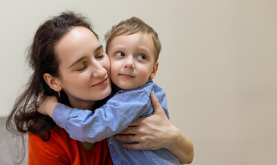 Loving mother hugging her young son. A loving mother embraces her young son with a warm hug, eyes closed in happiness, while he looks away with a shy smile.