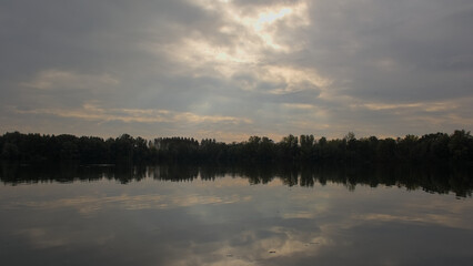Lake with tree silhouettes reflecting in the water under a dark stormy sky in Damvallei nature reserve, Ghent, Flanders, Belgium 