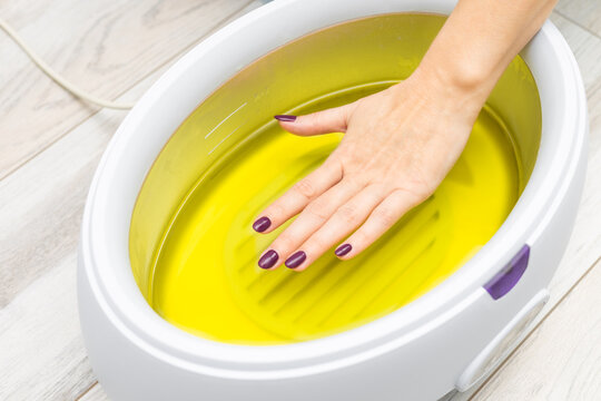 a woman's hand is dipped into melted paraffin.  female hand immersed in paraffin bath. woman doing paraffin therapy for hands, close-up. wax machine for paraffin therapy. spa manicure procedure. 