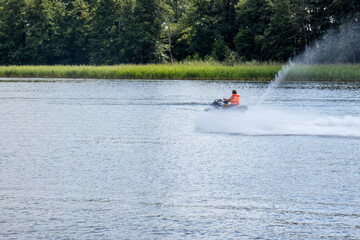 A man riding a jet ski on a calm lake, surrounded by green trees, creating splashes of water. A peaceful summer activity
