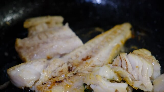 Cooking Indoors pan grilled seasoned Cod fillets on Stovetop, iron cast pan, close up boiled oil,   sprinkle with soy sauce. White meat