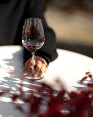 Bordeaux glass with red wine in hand on table. Ruby wine in burgundy wineglass. Wine tasting. Aperitif. Alcohol beverage. Drink concept. Copy space. Warm autumn atmosphere. Dinner in restaurant.
