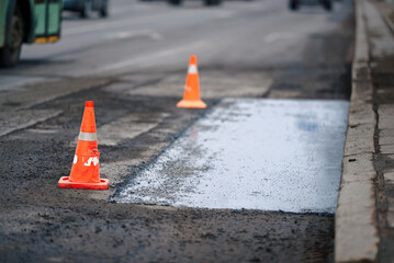 Pothole repair, traffic cones marking repaired asphalt section. Repairing pothole with fresh...
