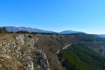 Railroad and a train bellow the limestone cliffs at Karst edge and Slavnik mountain above in Primorska, Slovenia
