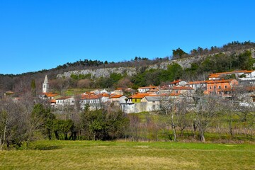 View of Črnotiče village bellow a rock wall with the church tower and a meadow in front at Karst in Istria, Primorska, Slovenia