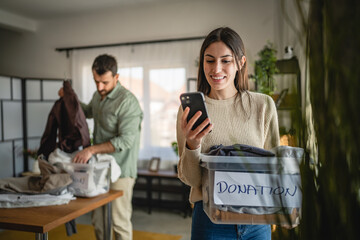 woman stand use mobile phone and hold box with clothes for donation
