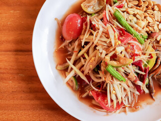 Top view papaya salad (Som Tam) Popular traditional Thai food with spicy flavors in white plate on wooden table, Close-up of illustration, concept for restaurant menu.