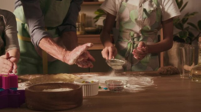 Midsection view of unknown grandmother teaching her grandson to sift flour through small metal sieve when his sister and he preparing dough for sugar cookies